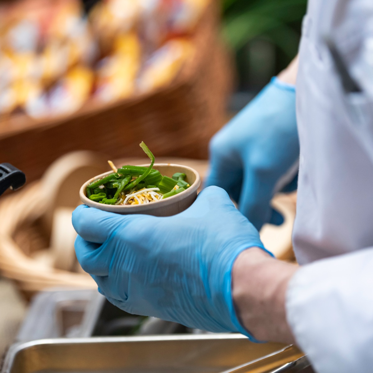 Gloved hands serve a cup of chili garnished with green onions and cheese on top