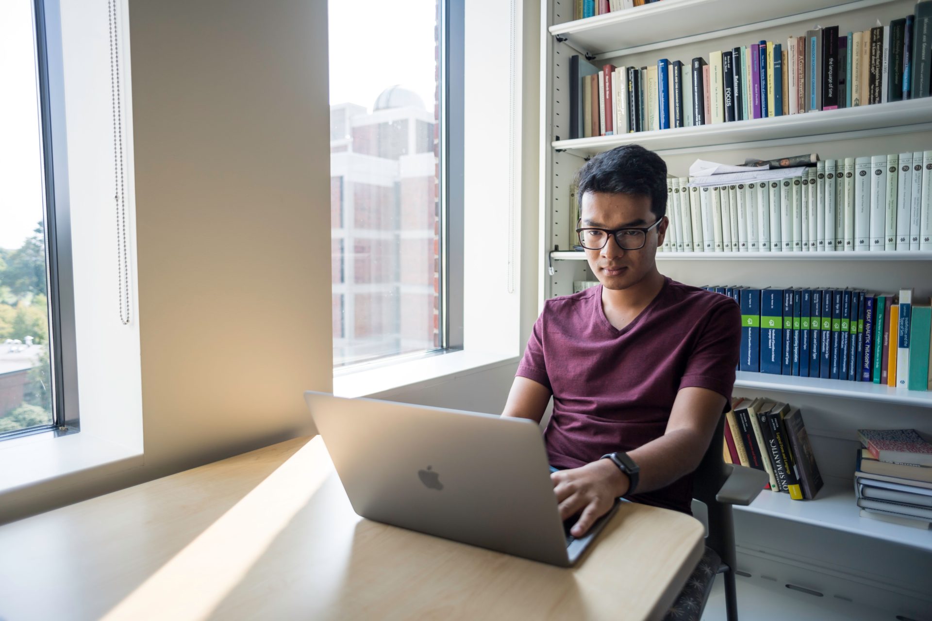 A University of Rochester graduate student in a library room on their laptop